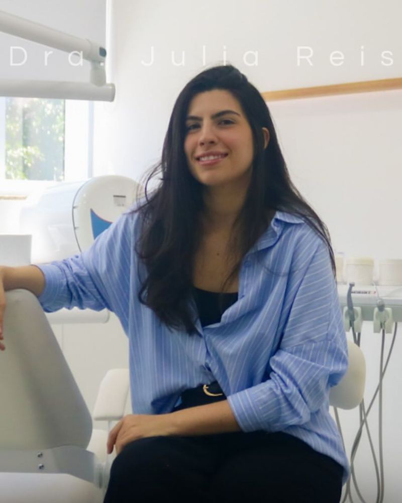 Dra. Júlia Reis, cirurgiã-dentista, sorrindo em seu consultório odontológico em Santana, São Paulo